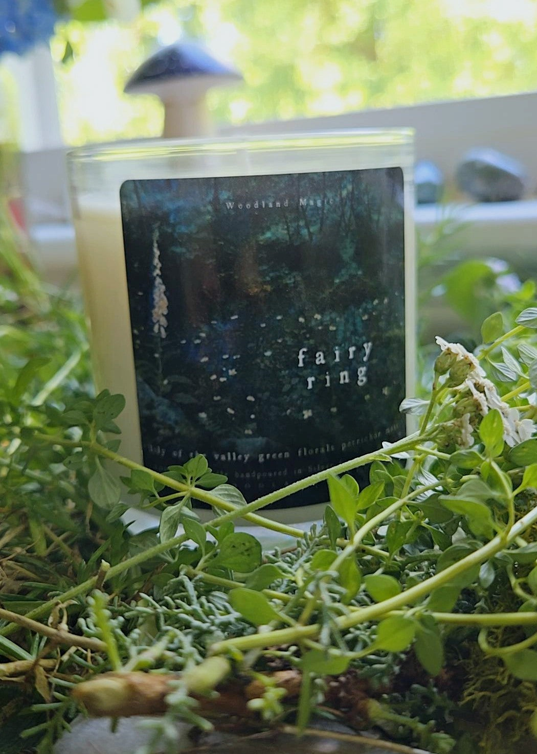 Candle labeled 'Fairy Ring' on a bed of greenery with mushroom decor