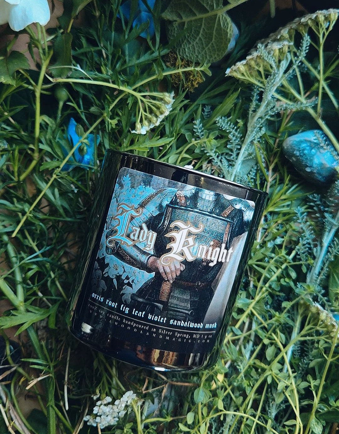 Candle labeled "lady knight" on a bed of green leaves and flowers