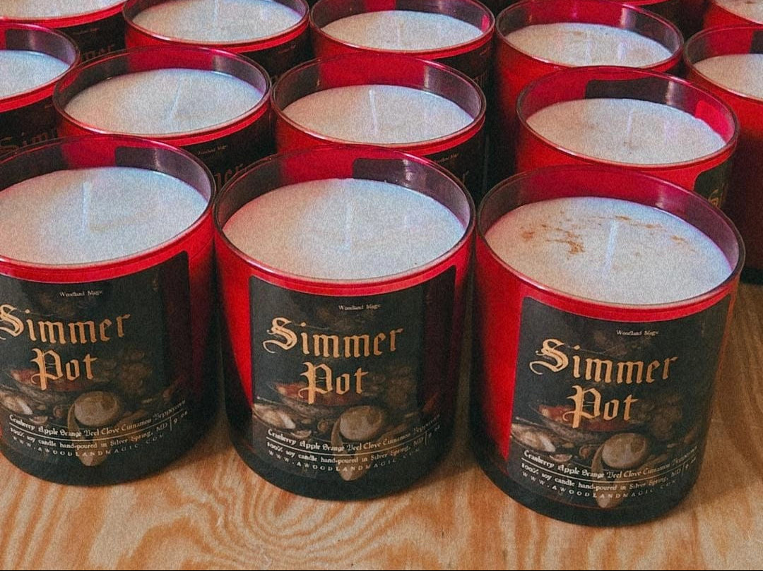 Multiple 'Simmer Pot' candles on a wooden surface with a workshop background.
