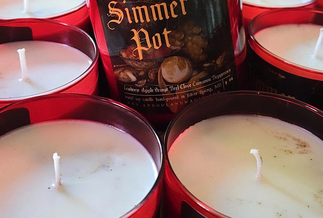 Hand holding a 'Simmer Pot' candle among other similar candles.